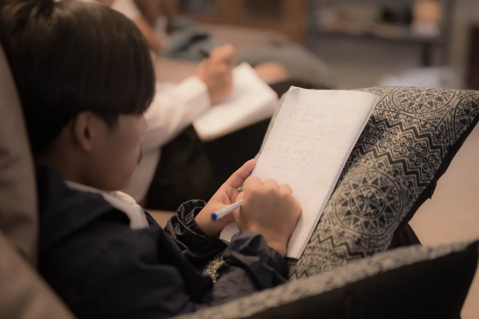Estudiante joven escribiendo en un cuaderno, sentado en un sillón