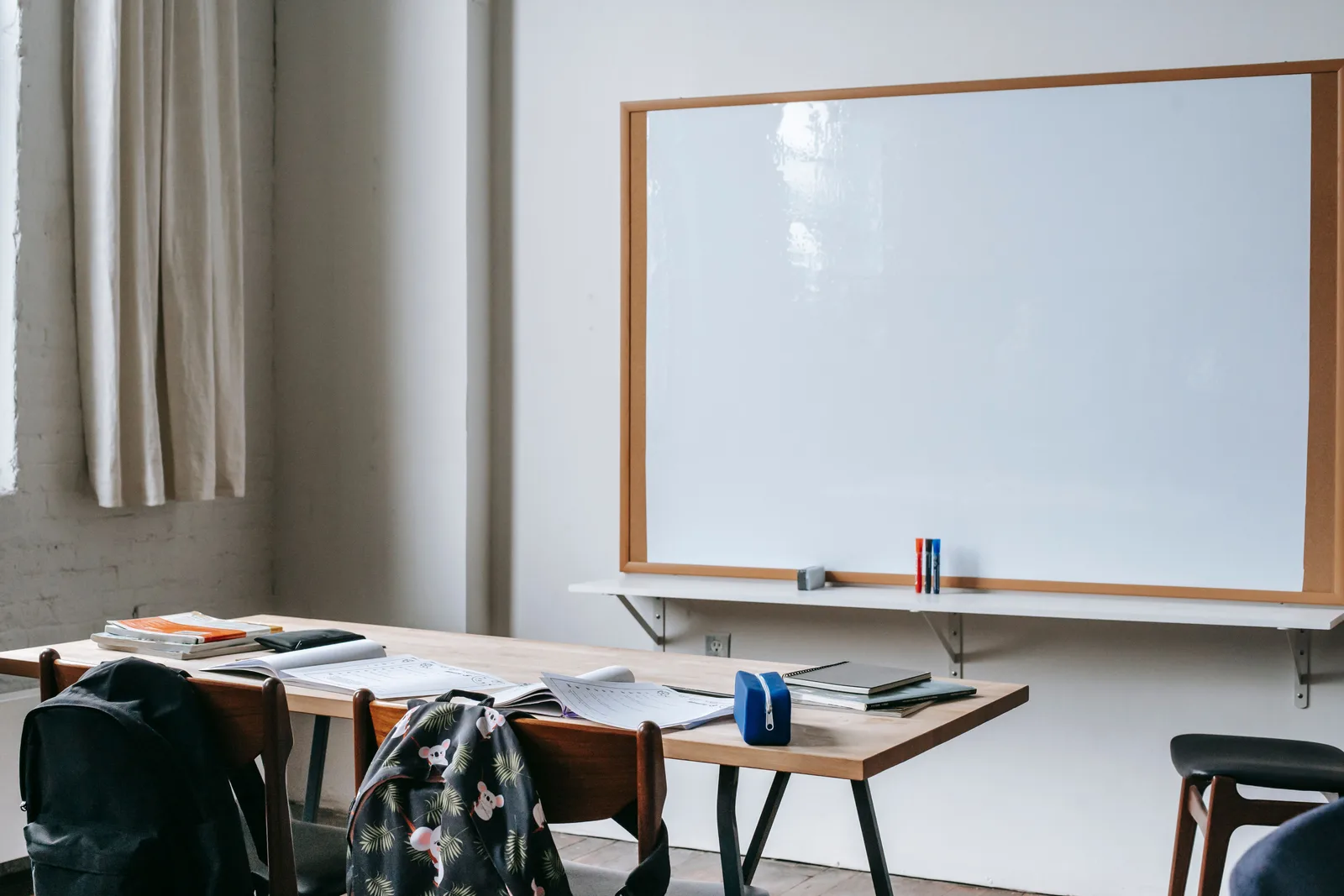 Aula con cuadernos de ejercicios abiertos sobre la mesa y una pizarra al fondo
