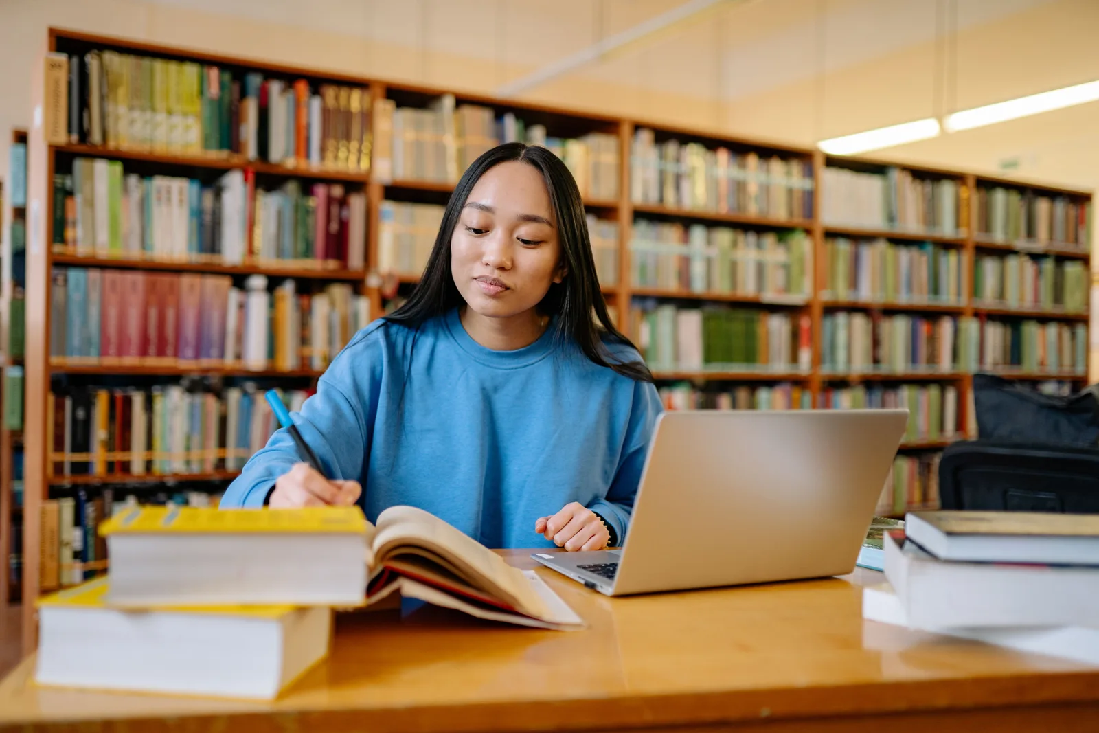 Estudiante tomando notas entre libros y un portátil en una biblioteca universitaria
