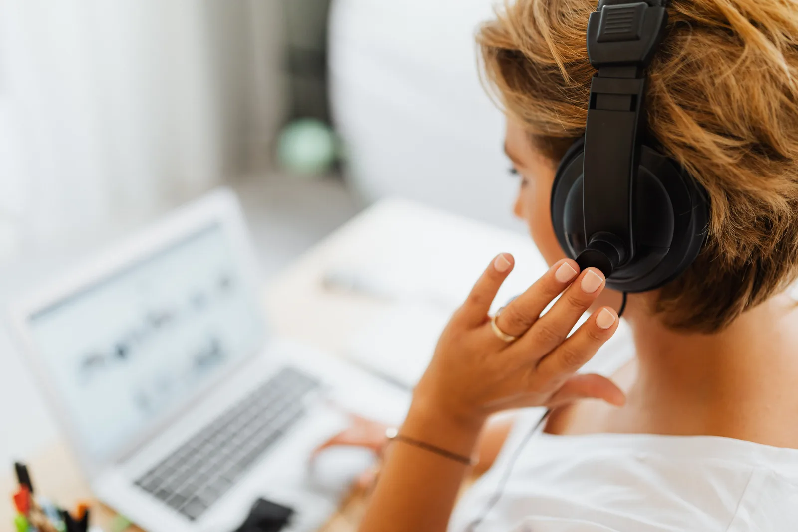 Persona con auriculares y un portátil, ajustándose el casco durante una escucha
